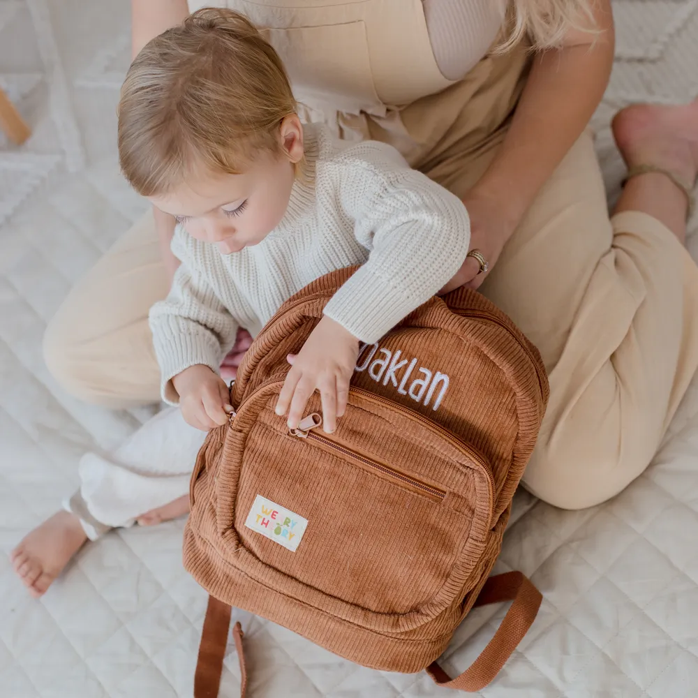 Child sitting with mother holding the Chocolate Corduroy Backpack