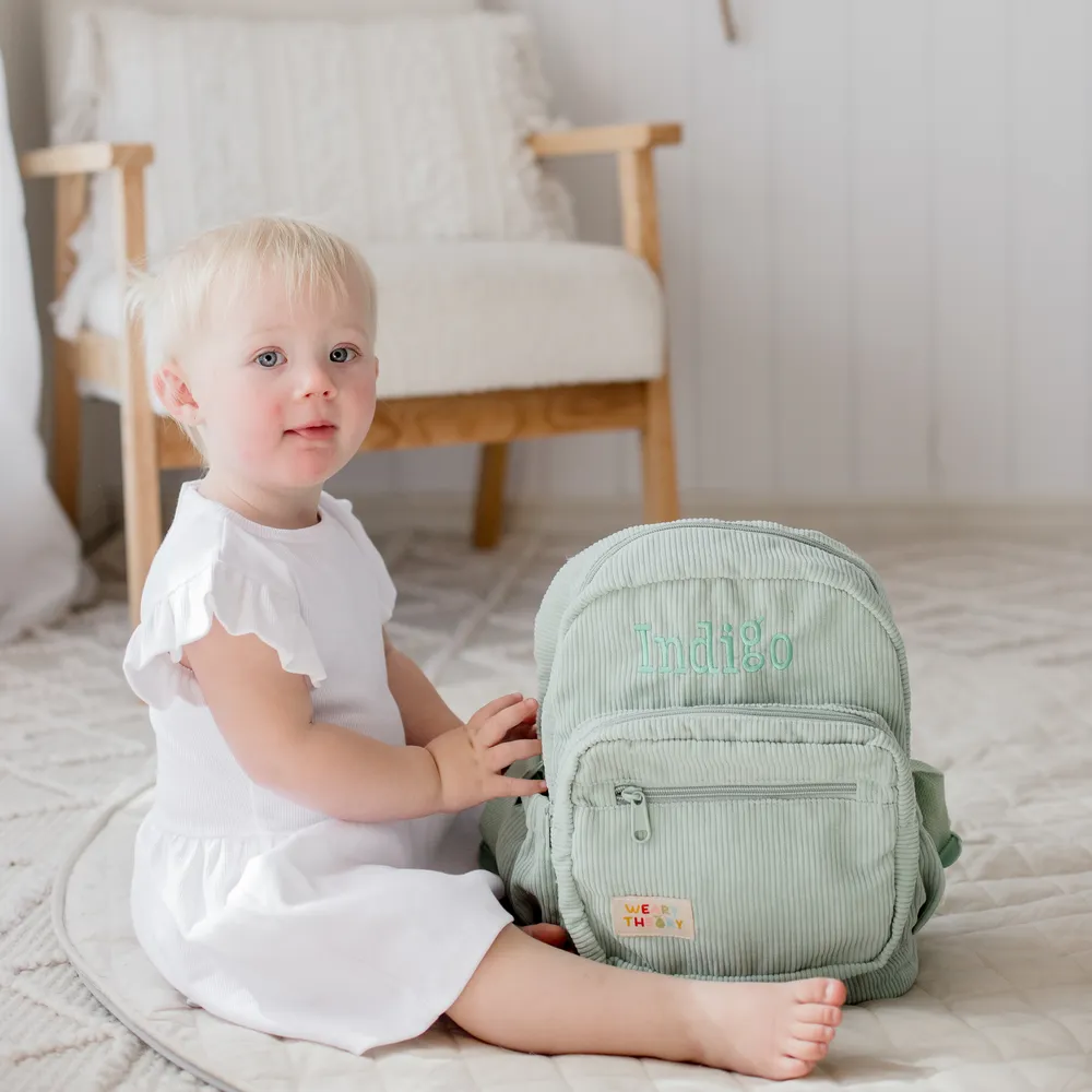 Child sitting next to Pear Corduroy Backpack