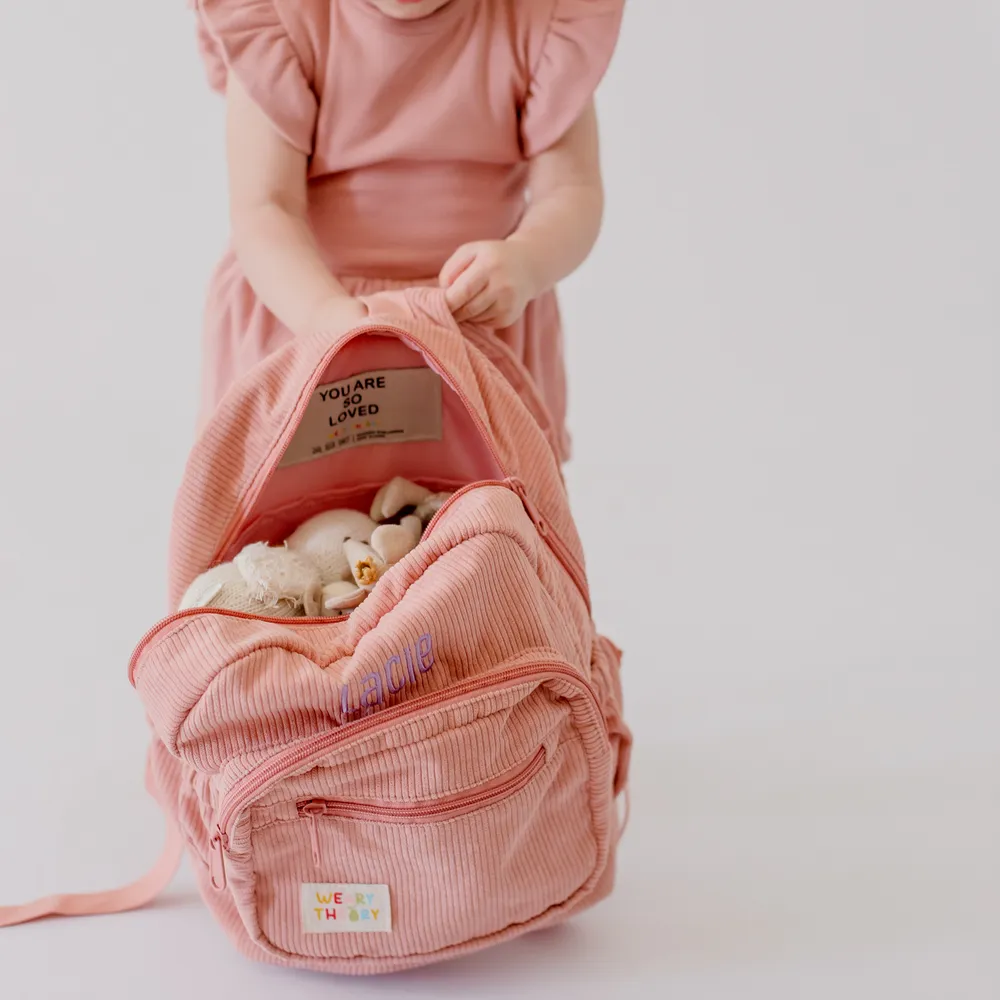 Child holding the Strawberry Corduroy Backpack filled with soft toys